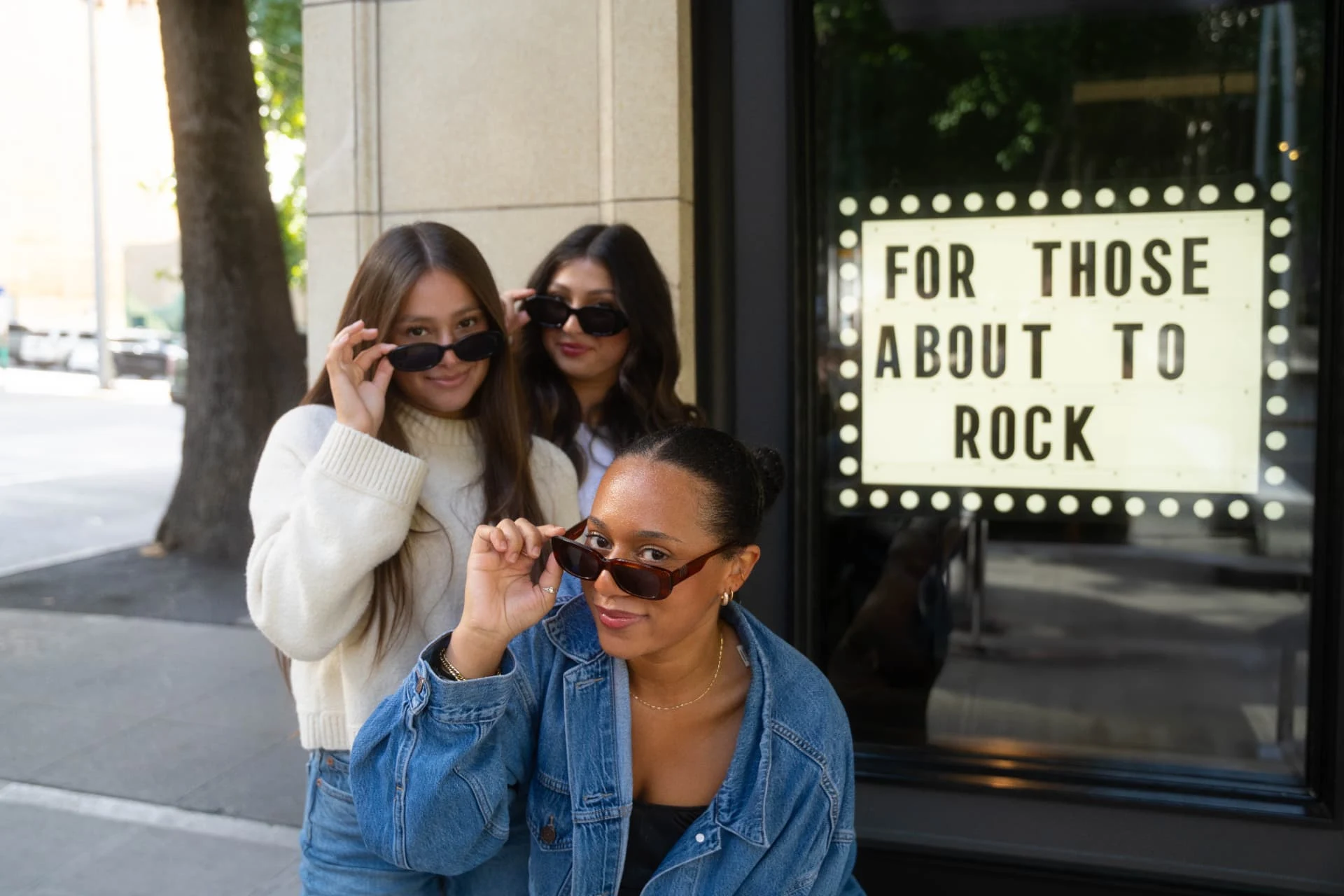 Three friends in sunglasses beside a marquee sign