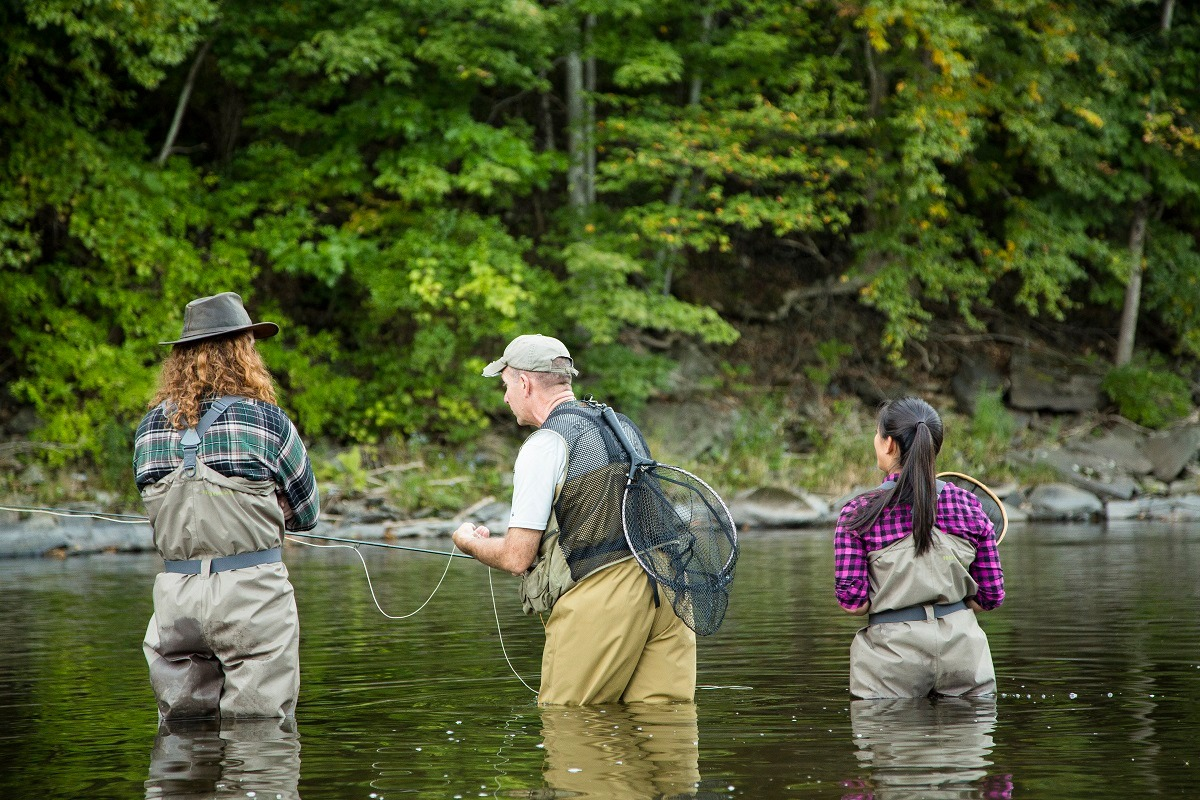 Three anglers fly fishing in a tree-lined river