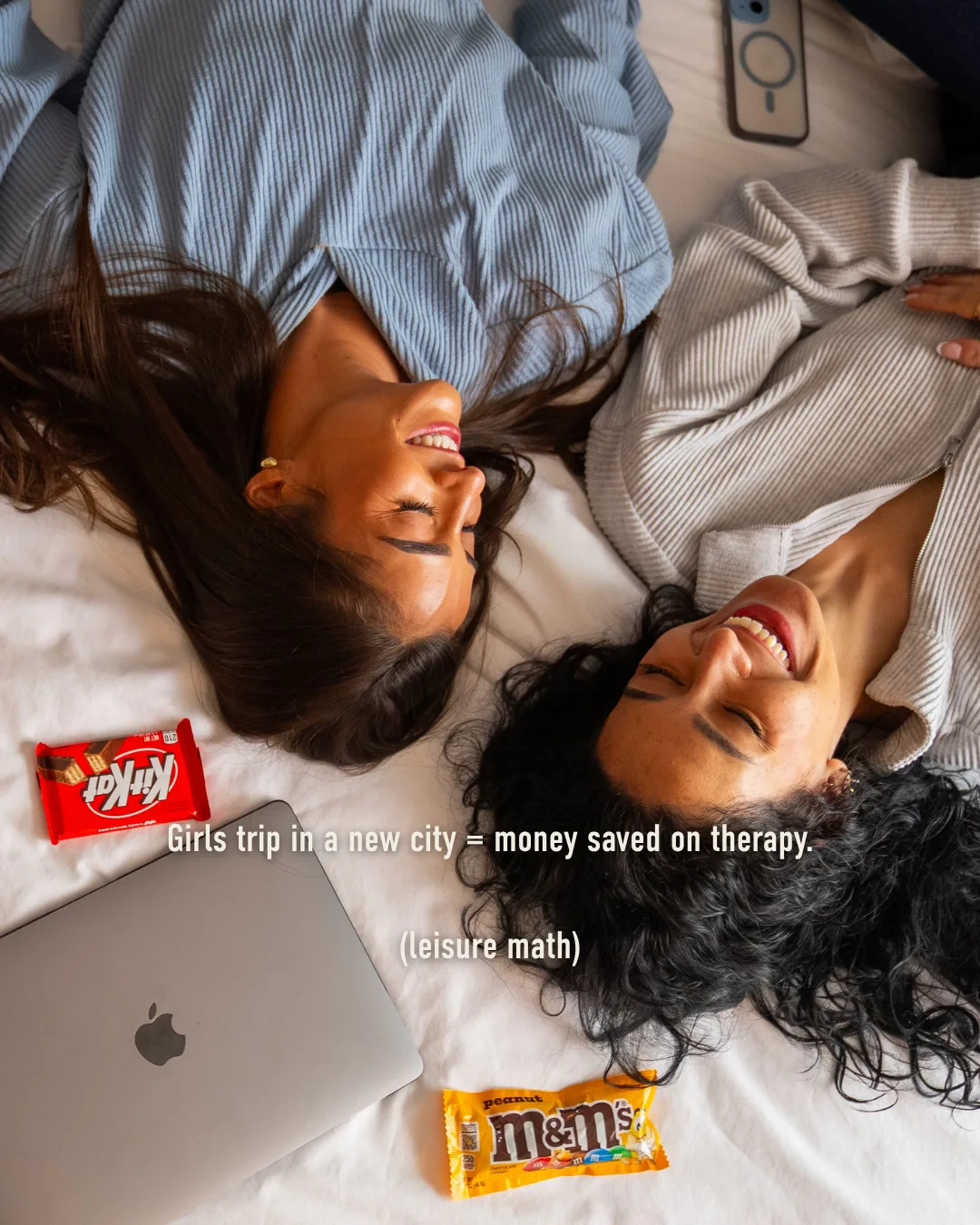 Friends laughing on a hotel bed: a girls trip in a new city is money saved on therapy