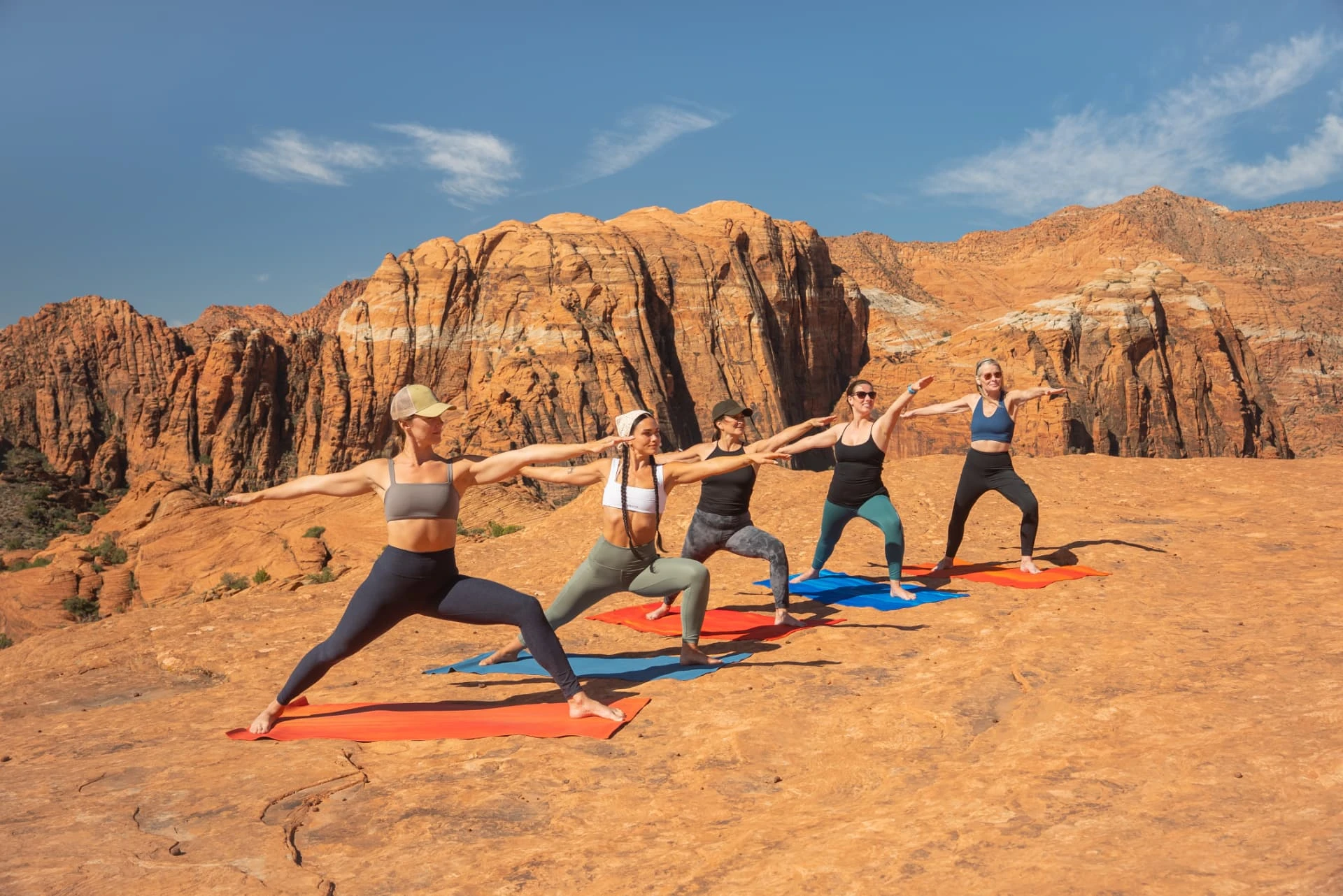 Five guests holding a yoga pose on red sandstone beneath desert cliffs